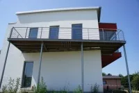 Balkon auf Stahlstützen mit Geländer aus Edelstahl an einem weißen Neubau.