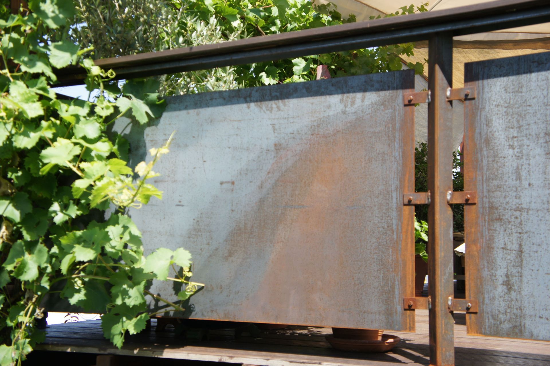 Sichtschutzwand aus Cortenstahl-Platten mit rostbrauner Patina an Stahlpfosten, auf einer Terrasse mit Weinranken.