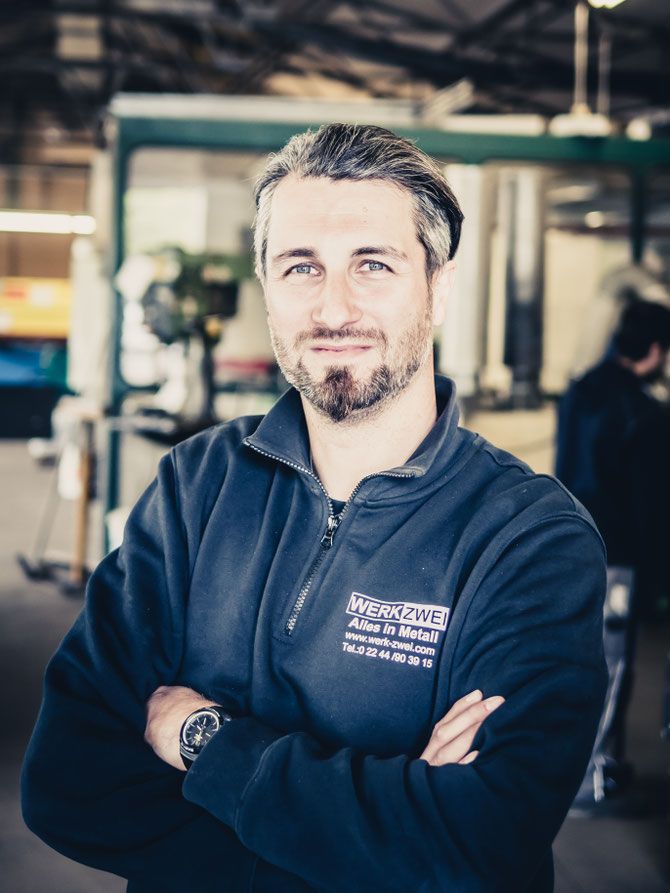 Markus Sülzen mit verschränkten Armen, im Pullover mit dem Logo WERK ZWEI, in der Werkhalle.
