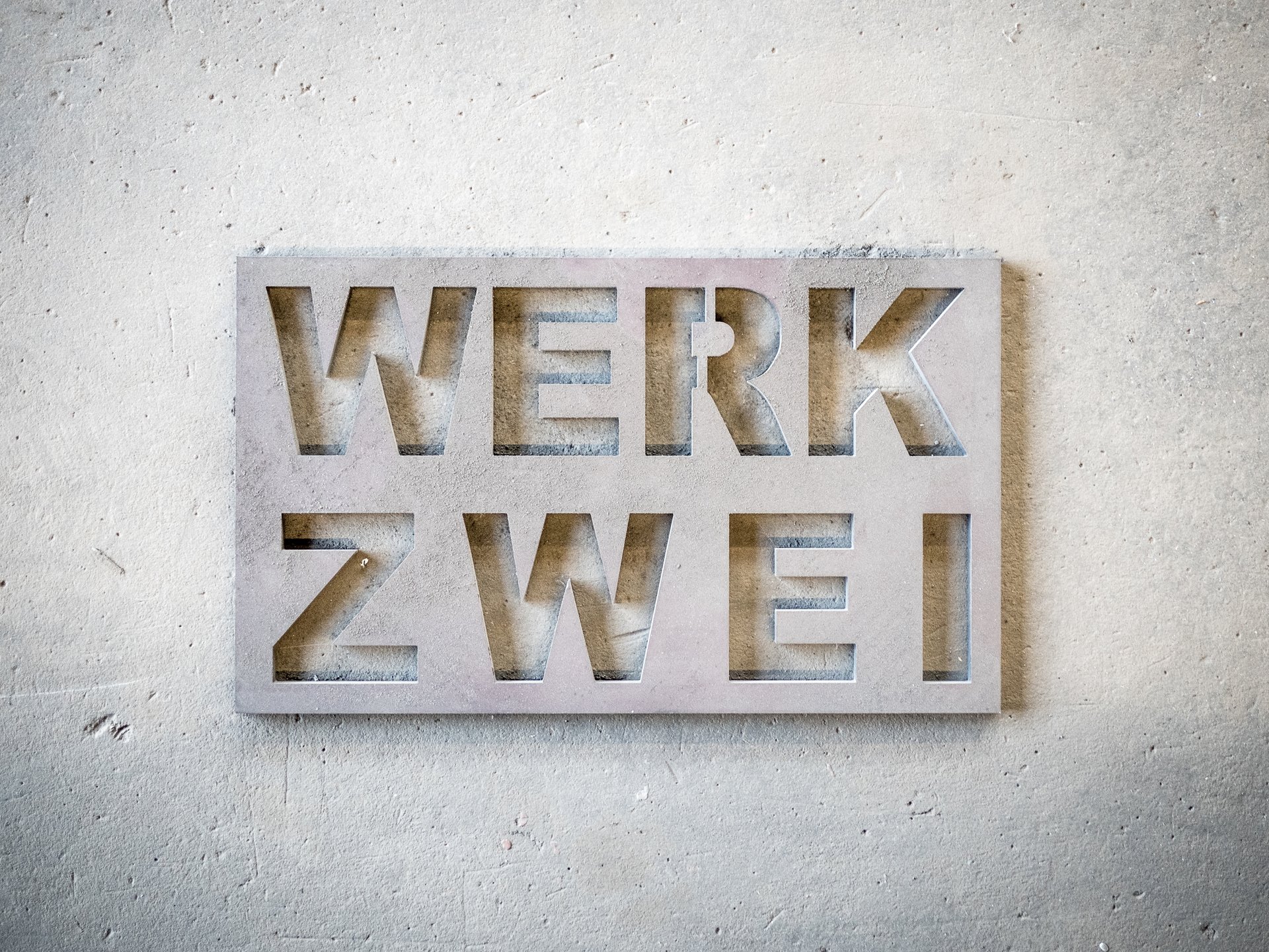 Aus Stahlblech ausgeschnittenes Firmenschild WERK ZWEI an einer Sichtbetonwand.
