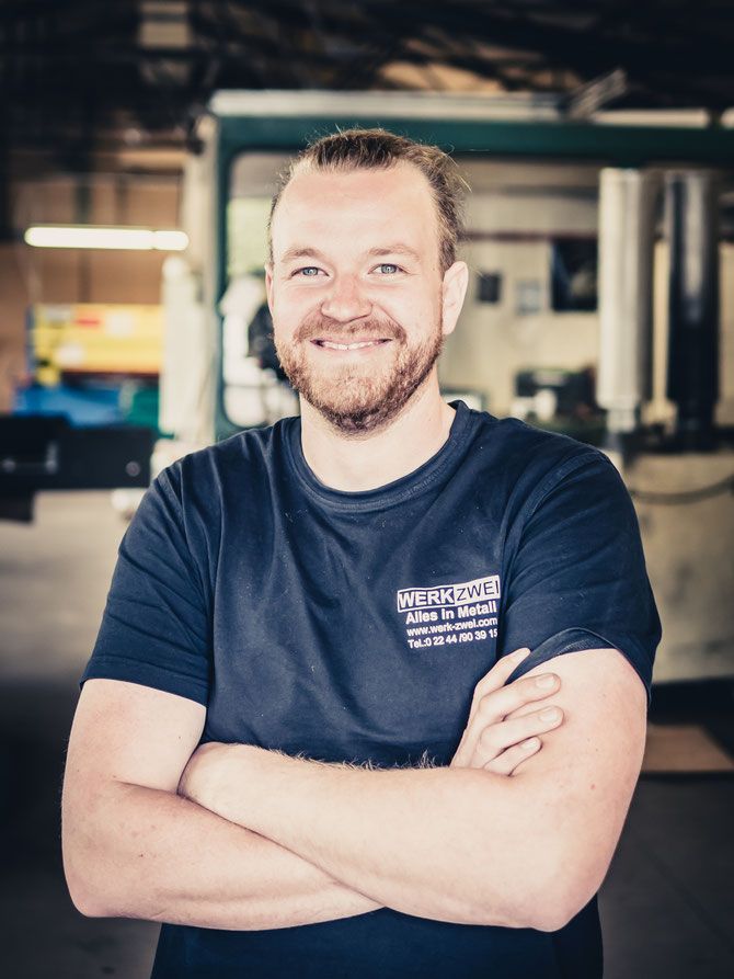 Nils Berg mit verschränkten Armen, im T-Shirt mit Firmenlogo, in der Werkhalle.